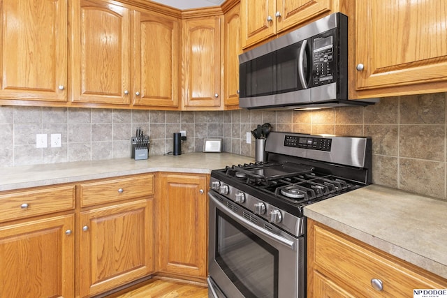 kitchen with light wood-style flooring, backsplash, appliances with stainless steel finishes, brown cabinetry, and light countertops