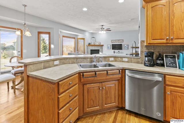 kitchen featuring a peninsula, a sink, light countertops, stainless steel dishwasher, and ceiling fan with notable chandelier