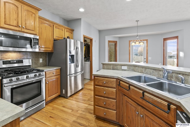 kitchen with a sink, decorative backsplash, stainless steel appliances, decorative light fixtures, and light wood-type flooring