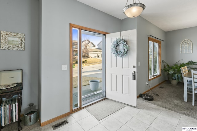 foyer entrance featuring light tile patterned flooring, visible vents, light colored carpet, and baseboards