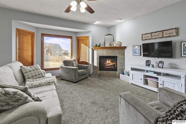 living room featuring a tiled fireplace, carpet flooring, a ceiling fan, and a textured ceiling