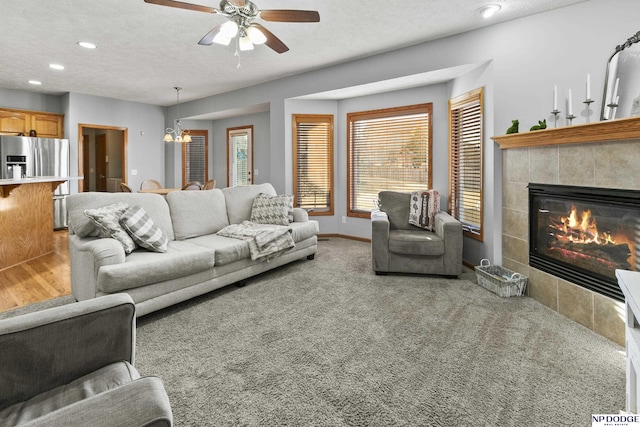 carpeted living room featuring a textured ceiling, ceiling fan with notable chandelier, recessed lighting, and a tile fireplace