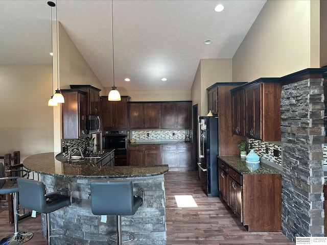 kitchen with dark stone countertops, freestanding refrigerator, dark wood-type flooring, stainless steel microwave, and backsplash