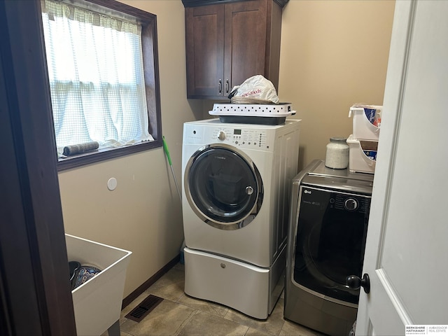 clothes washing area featuring visible vents, baseboards, light tile patterned floors, washer and dryer, and cabinet space