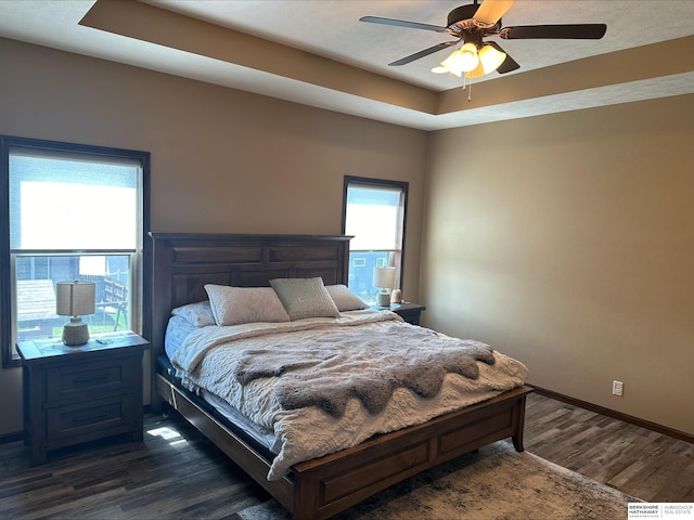 bedroom with dark wood finished floors, a tray ceiling, baseboards, and ceiling fan