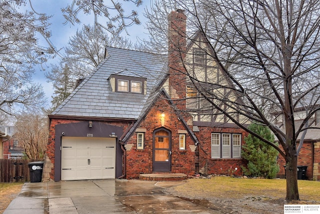 tudor-style house featuring a high end roof, concrete driveway, an attached garage, brick siding, and a chimney