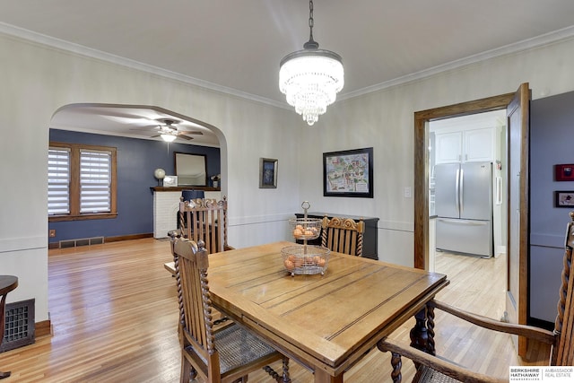 dining room with crown molding, visible vents, arched walkways, and light wood-type flooring