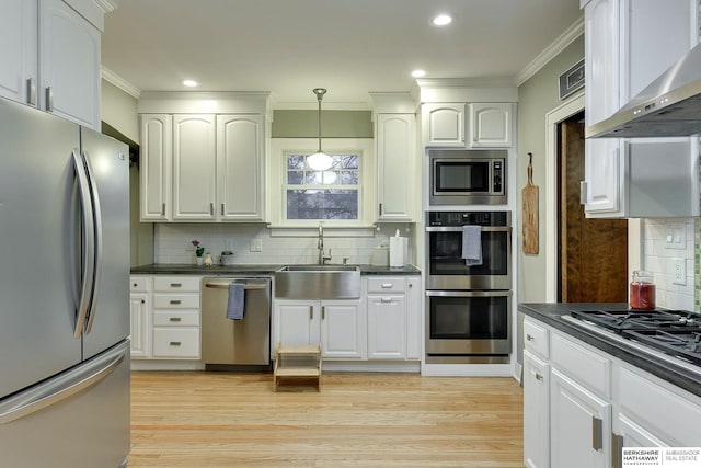 kitchen featuring dark countertops, appliances with stainless steel finishes, wall chimney exhaust hood, and a sink