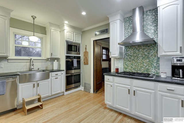 kitchen with dark countertops, appliances with stainless steel finishes, wall chimney exhaust hood, and a sink