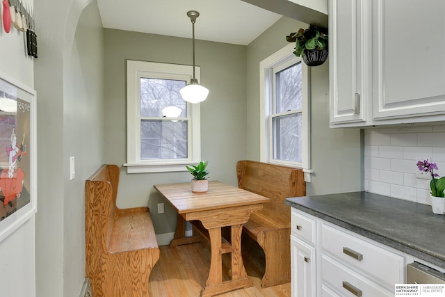 dining space with a wealth of natural light, light wood-style flooring, arched walkways, and baseboards