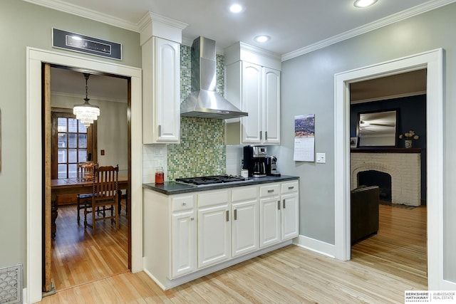 kitchen featuring dark countertops, wall chimney range hood, stainless steel gas cooktop, light wood-style floors, and white cabinets