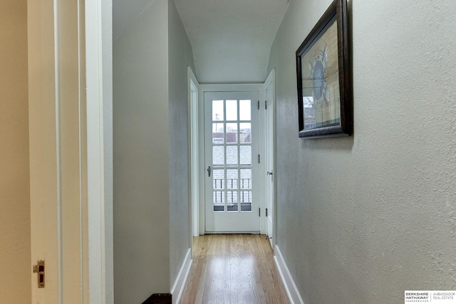 doorway to outside featuring wood finished floors, a textured wall, and baseboards