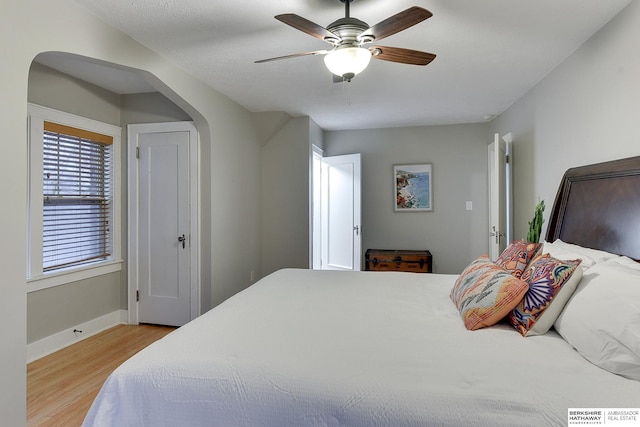 bedroom with arched walkways, a ceiling fan, light wood-type flooring, and baseboards