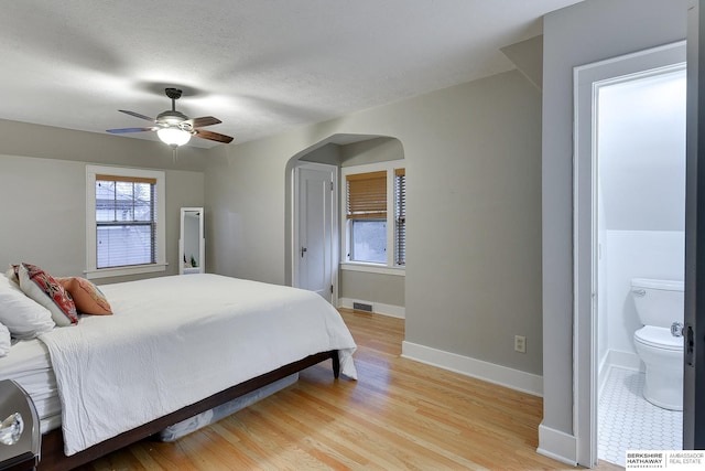 bedroom with visible vents, connected bathroom, baseboards, light wood-style flooring, and arched walkways