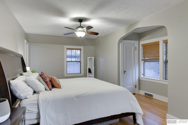 bedroom featuring wood finished floors, baseboards, visible vents, arched walkways, and a textured ceiling