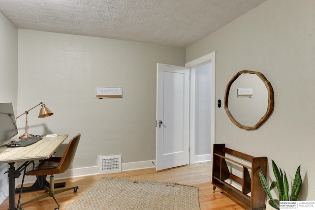 home office featuring visible vents, a textured ceiling, light wood-style floors, and baseboards