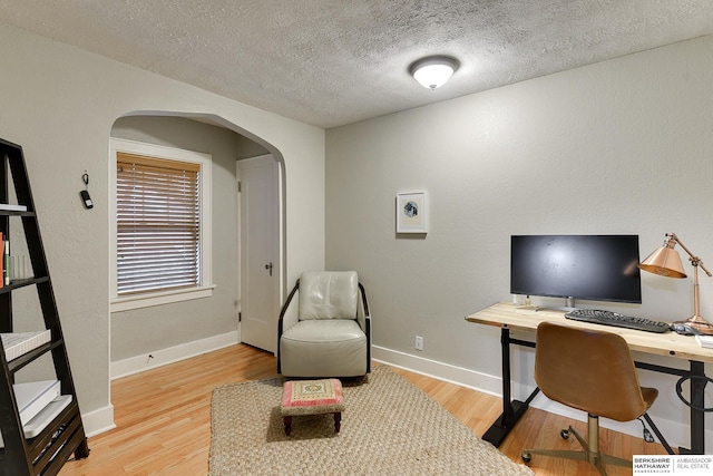 home office featuring a textured ceiling, arched walkways, light wood-type flooring, and baseboards