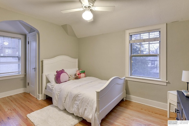 bedroom featuring arched walkways, multiple windows, baseboards, and light wood-style floors