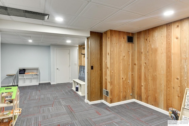 finished below grade area featuring wooden walls, visible vents, baseboards, and carpet floors