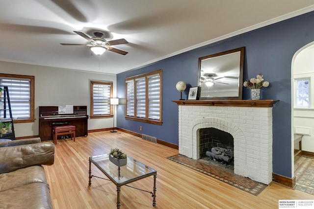 living room featuring wood finished floors, plenty of natural light, a brick fireplace, and ornamental molding