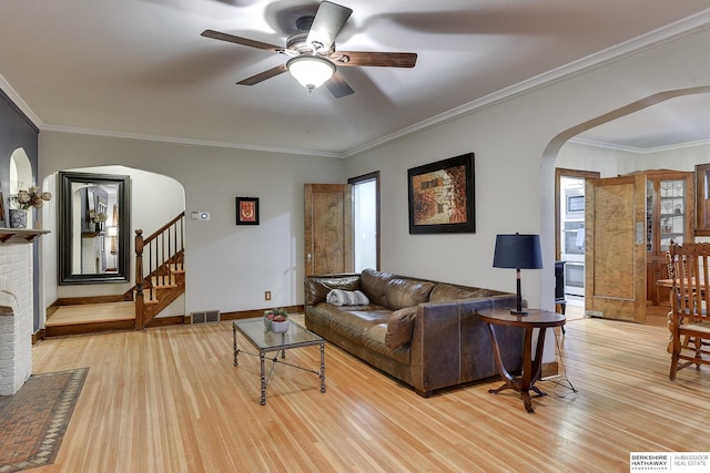 living room featuring visible vents, light wood finished floors, arched walkways, ornamental molding, and stairs