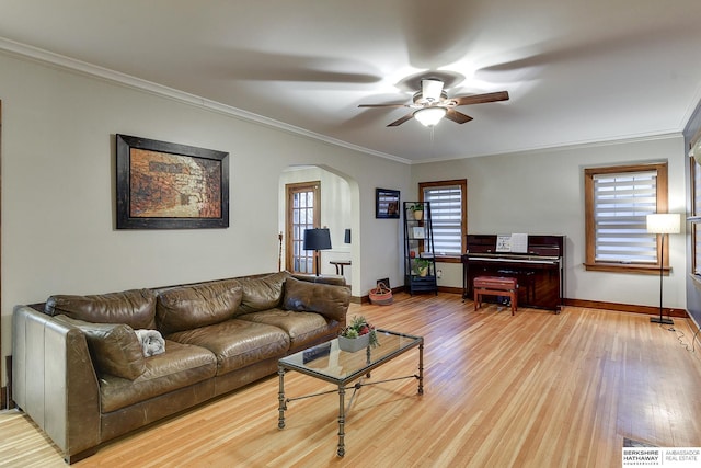 living room featuring crown molding, ceiling fan, baseboards, wood finished floors, and arched walkways