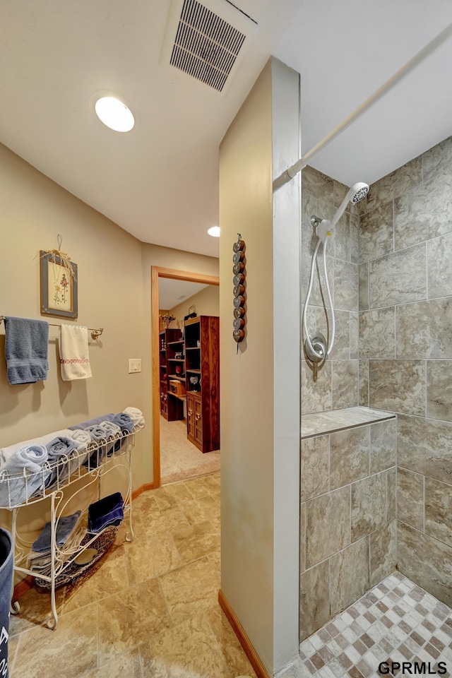 bathroom with visible vents, baseboards, a walk in closet, and a tile shower