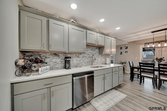 kitchen featuring decorative backsplash, gray cabinets, stainless steel dishwasher, light wood-style floors, and a sink