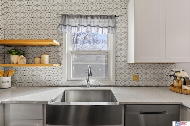 kitchen with a sink, backsplash, light stone countertops, and stainless steel dishwasher