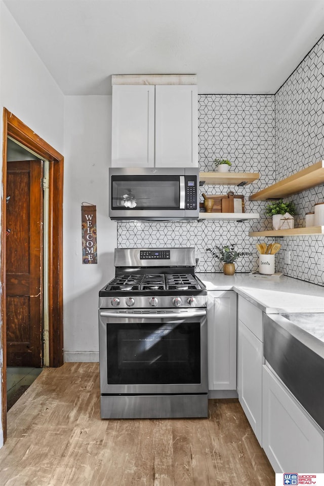 kitchen with open shelves, tasteful backsplash, white cabinetry, stainless steel appliances, and light countertops