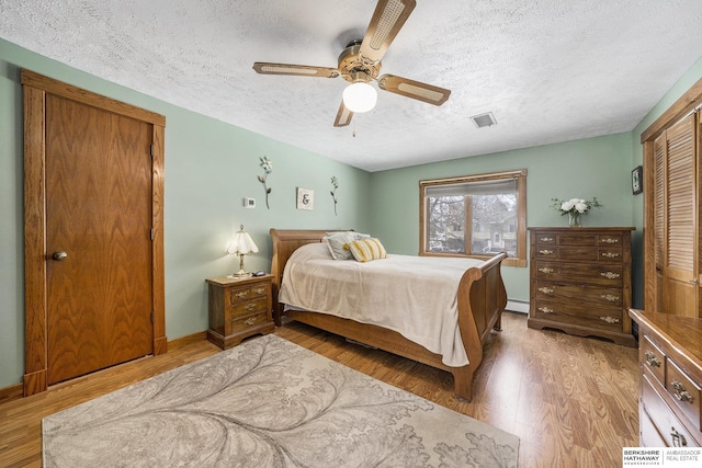 bedroom featuring visible vents, ceiling fan, baseboard heating, light wood-style flooring, and a textured ceiling