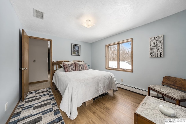 bedroom featuring visible vents, baseboards, baseboard heating, wood finished floors, and a textured ceiling