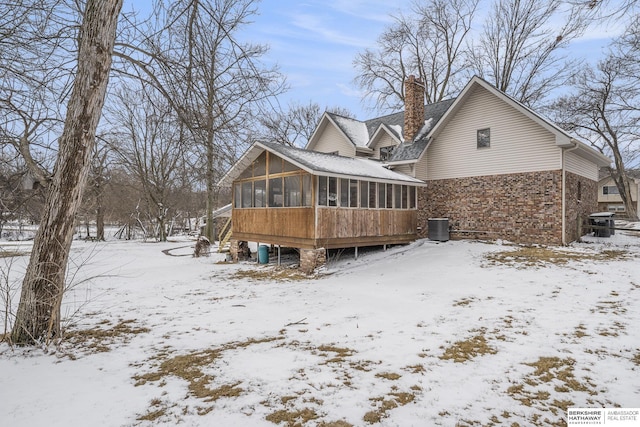 snow covered property featuring cooling unit, a chimney, and a sunroom