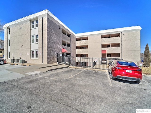 view of property with uncovered parking, central AC, and fence