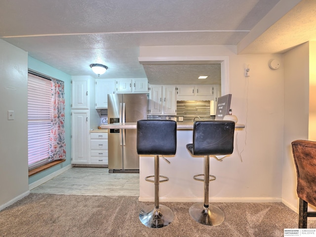 kitchen featuring light colored carpet, a kitchen bar, stainless steel refrigerator with ice dispenser, white cabinets, and a textured ceiling