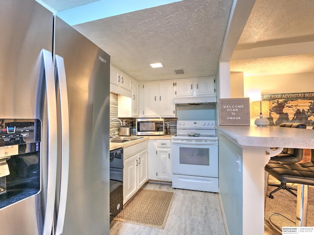 kitchen featuring light wood-style flooring, a sink, under cabinet range hood, a textured ceiling, and appliances with stainless steel finishes