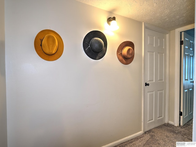 hallway featuring dark carpet, a textured ceiling, and baseboards