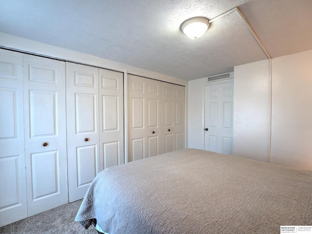 bedroom featuring multiple closets, carpet, visible vents, and a textured ceiling