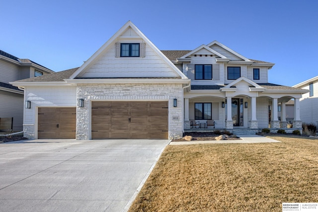 craftsman house featuring driveway, an attached garage, covered porch, a front lawn, and stone siding