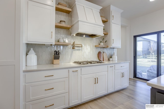 kitchen with open shelves, custom exhaust hood, light countertops, and stainless steel gas cooktop