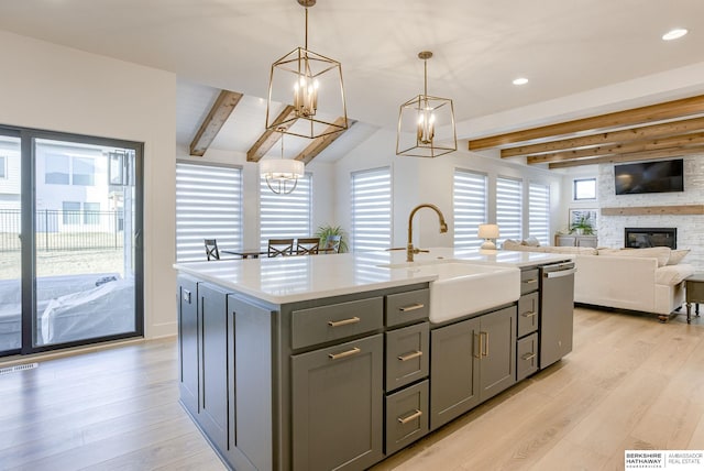 kitchen with light wood finished floors, a fireplace, gray cabinets, a sink, and stainless steel dishwasher