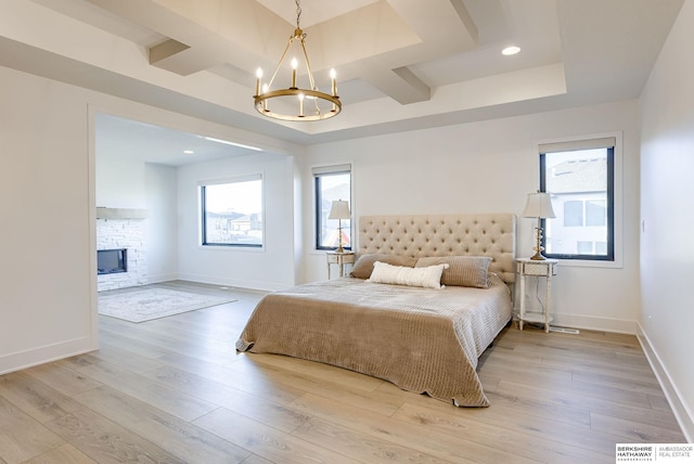 bedroom with a chandelier, a stone fireplace, multiple windows, and light wood-style floors