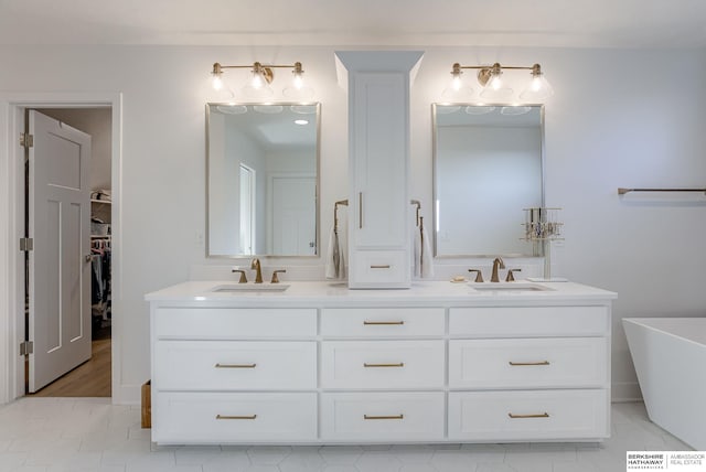 full bath with double vanity, a freestanding tub, a walk in closet, and a sink