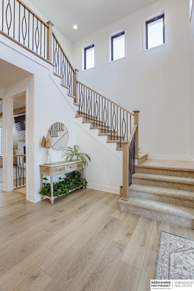 stairway featuring a high ceiling, recessed lighting, wood finished floors, and baseboards