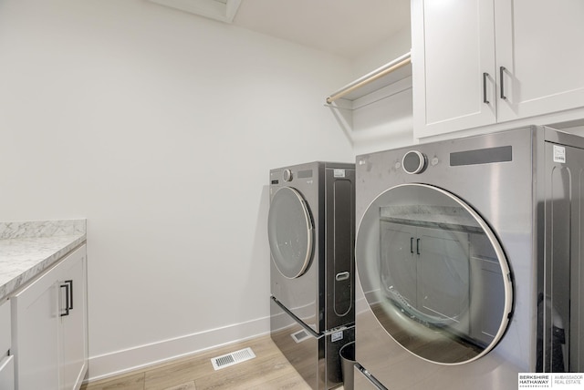 laundry room featuring visible vents, baseboards, cabinet space, light wood-style floors, and washing machine and dryer