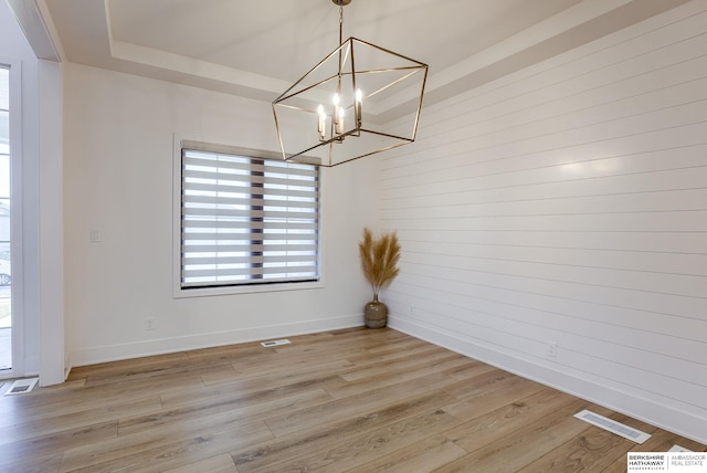 unfurnished dining area featuring a tray ceiling, visible vents, baseboards, and light wood-style flooring