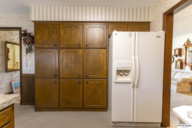 kitchen featuring white refrigerator with ice dispenser, light colored carpet, wallpapered walls, and light countertops