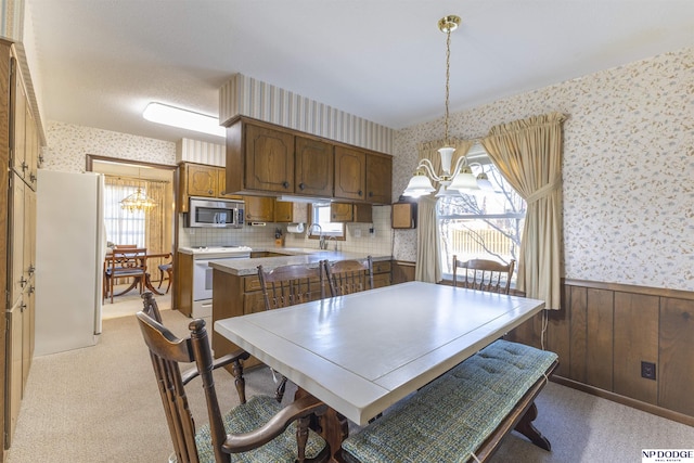 dining space with wallpapered walls, a notable chandelier, light colored carpet, and a wainscoted wall