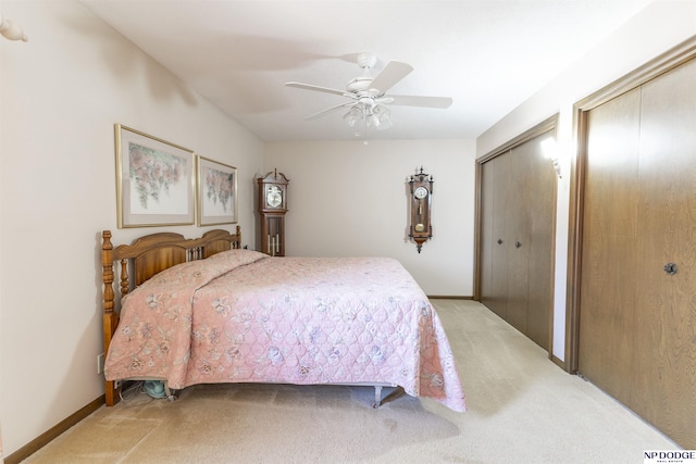 bedroom with a ceiling fan, light colored carpet, baseboards, and two closets