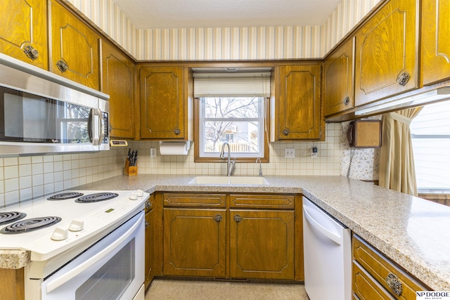 kitchen with wallpapered walls, white appliances, brown cabinetry, and a sink